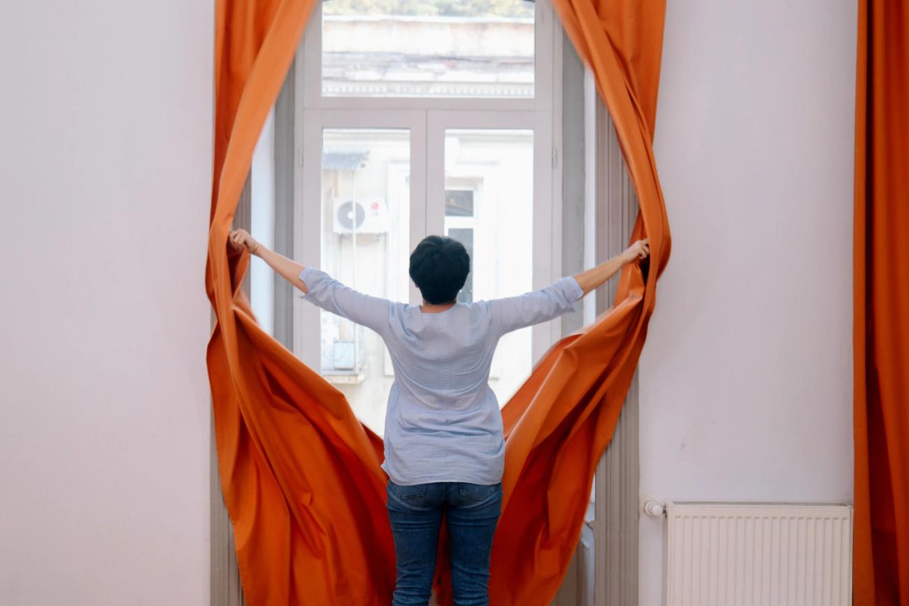 A Georgian woman opens a curtain.