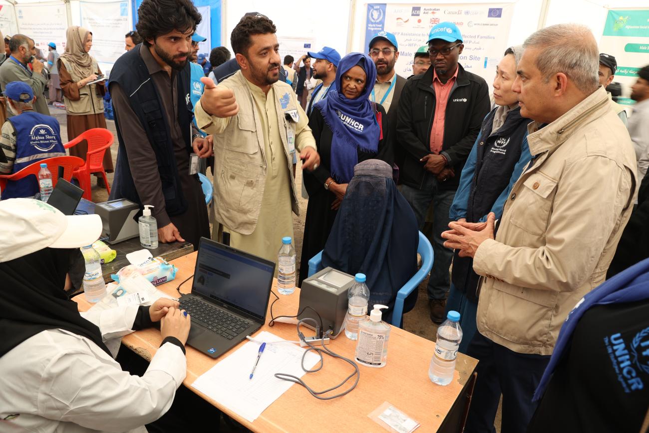 A man is asking another one a question, while there are crows around them. There is also a woman on a computer. 