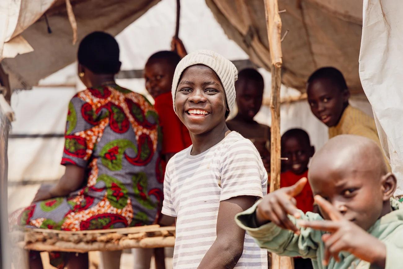 A young boy in Burundi smiles for a photo while surrounded by friends and siblings.
