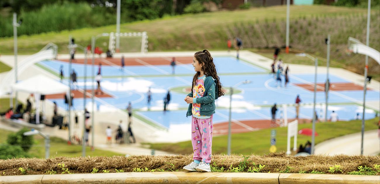 A girl in Costa Rica stands on a hill overlooking a basketball court.