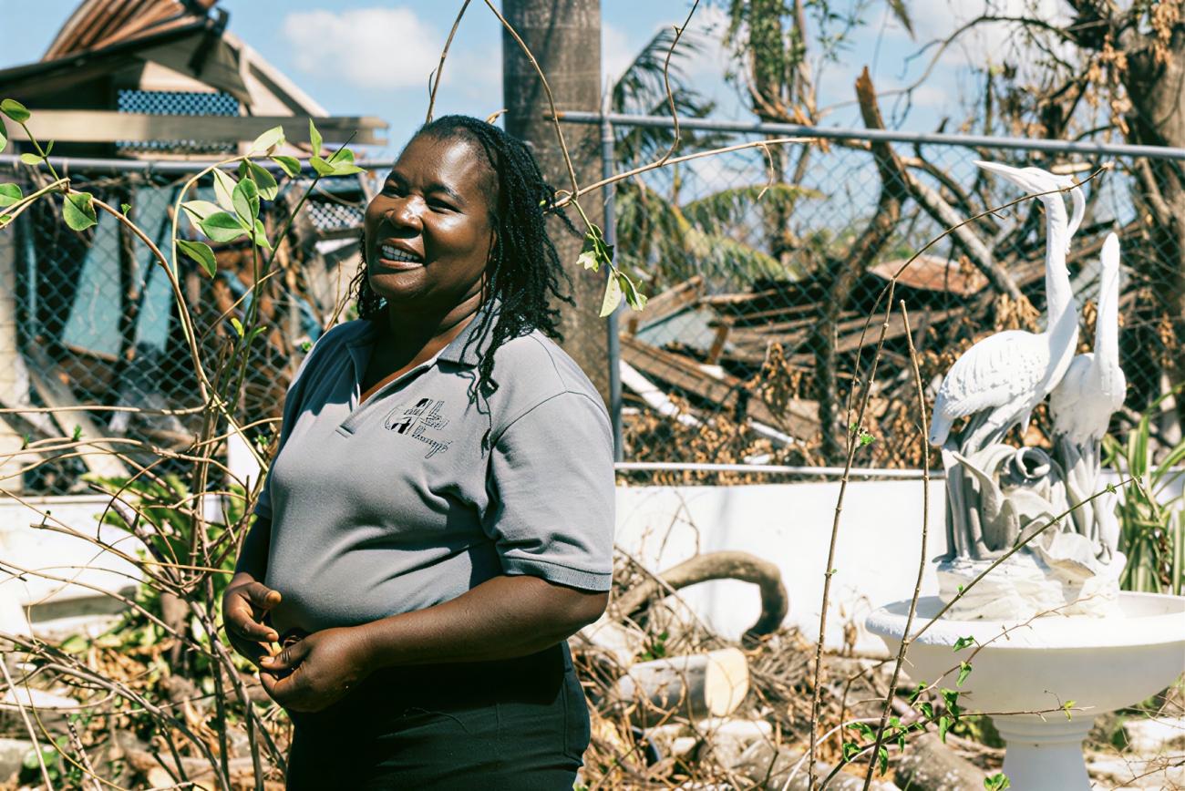 A woman in Jamaica stands in front of the destruction brought on by a hurricane.