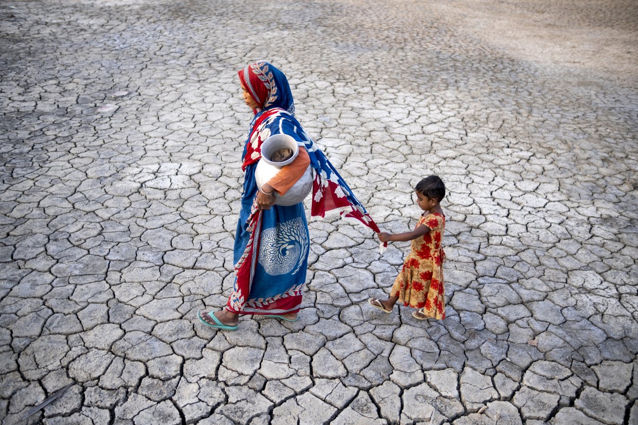 A woman in Bangladesh walks on drought-stricken land while holding her daughter's hand.