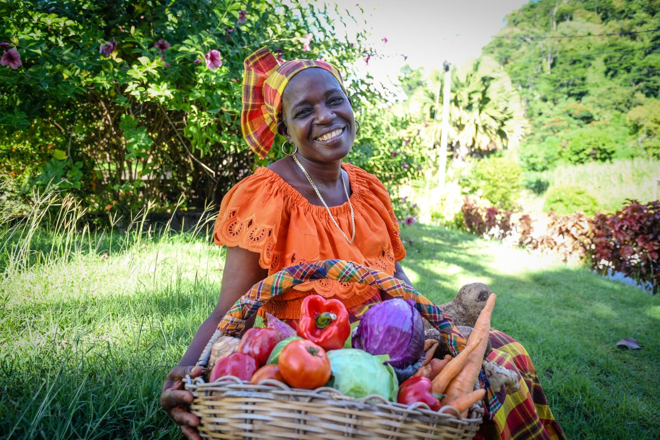 A woman in Dominica sits in front of a basket of food.