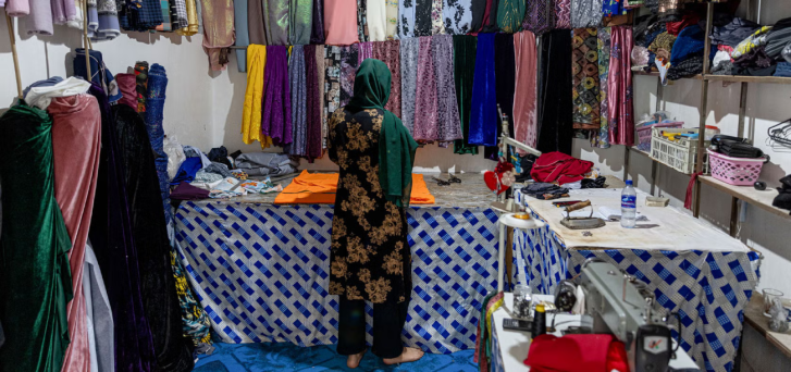 A woman is turning her back to the camera and looking through reams of cloth 