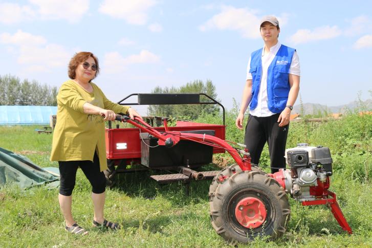 A Mongolian woman pushes a land mower in front of a man.
