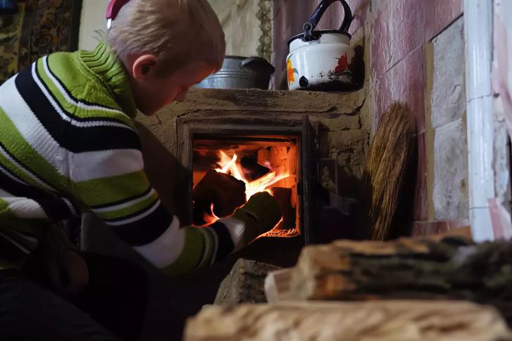 A boy in Ukraine puts wood in a wood heater.