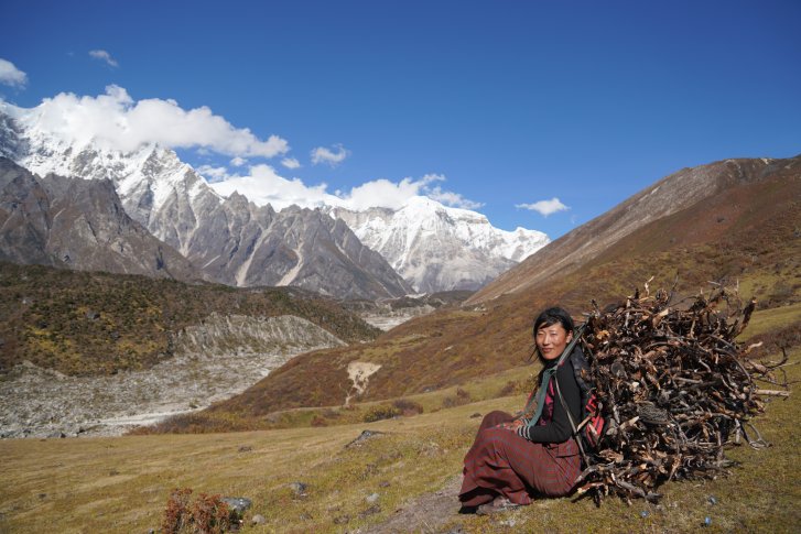 A woman in Bhutan sits on a hill overlooking a mountain range.