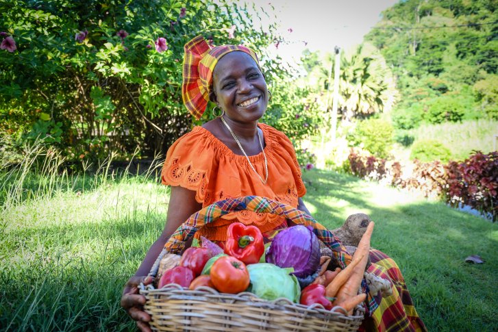 A woman in Dominica sits in front of a basket of food.