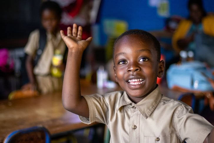 A young students raises his hand in a classroom in Jamaica.