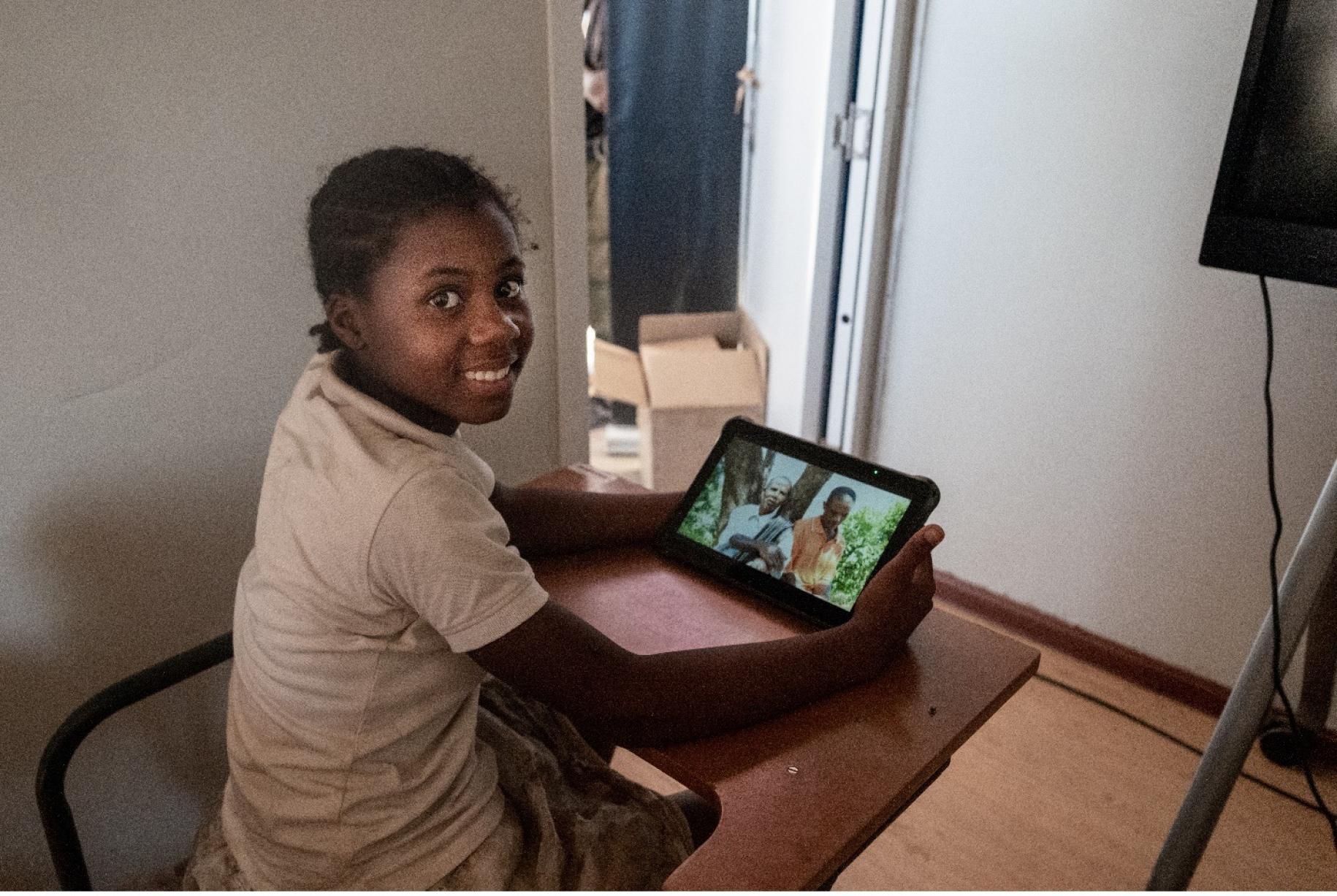 young girl sits at a desk using tablet