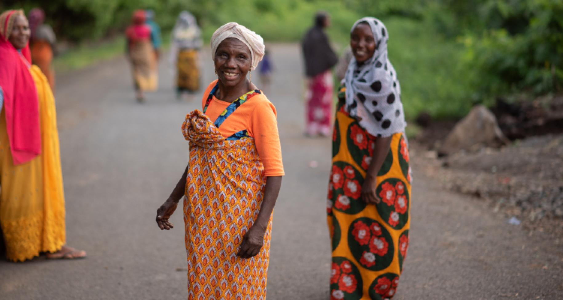 two woman in orange dress stand on road