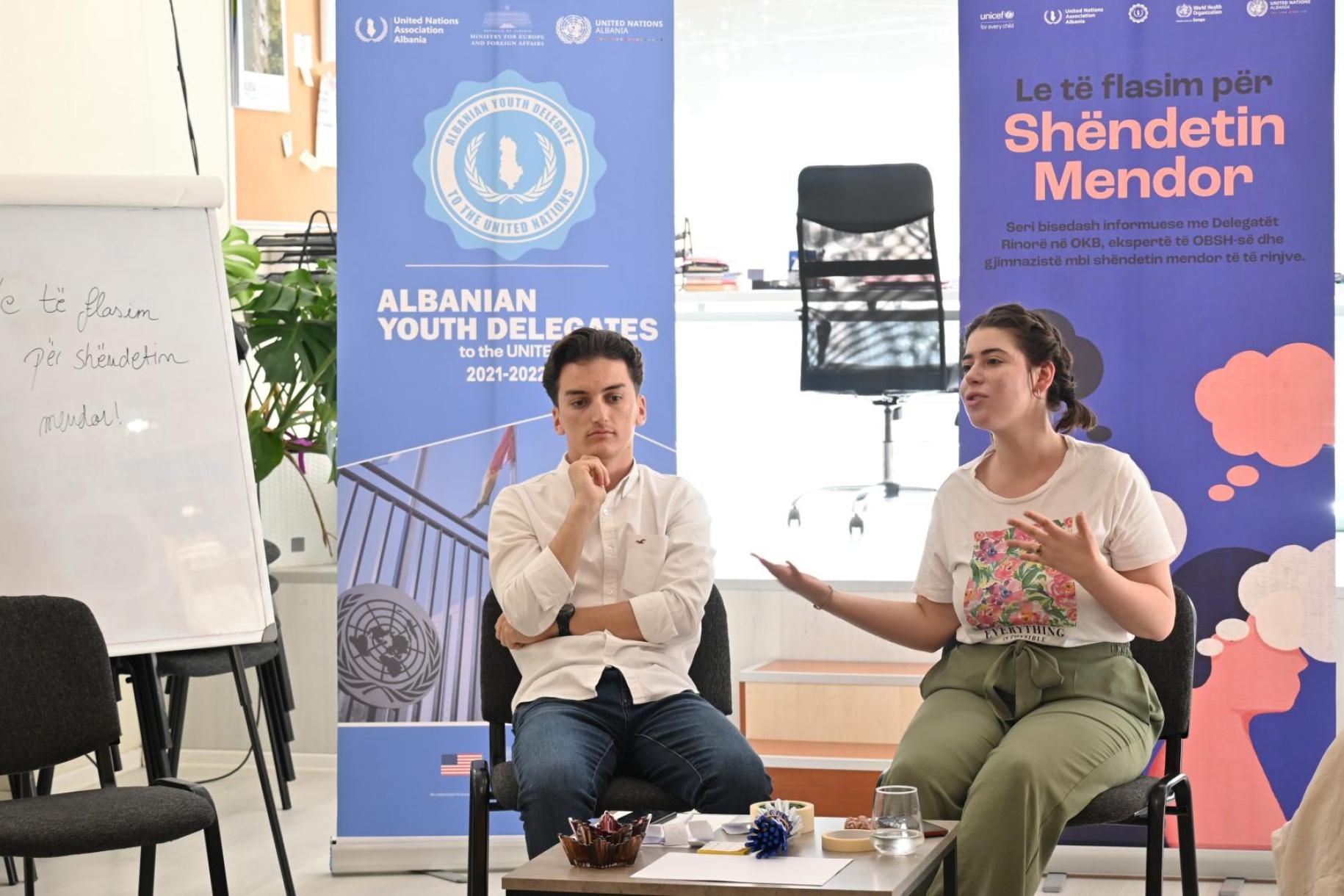 a young man and women sit on a stage talking