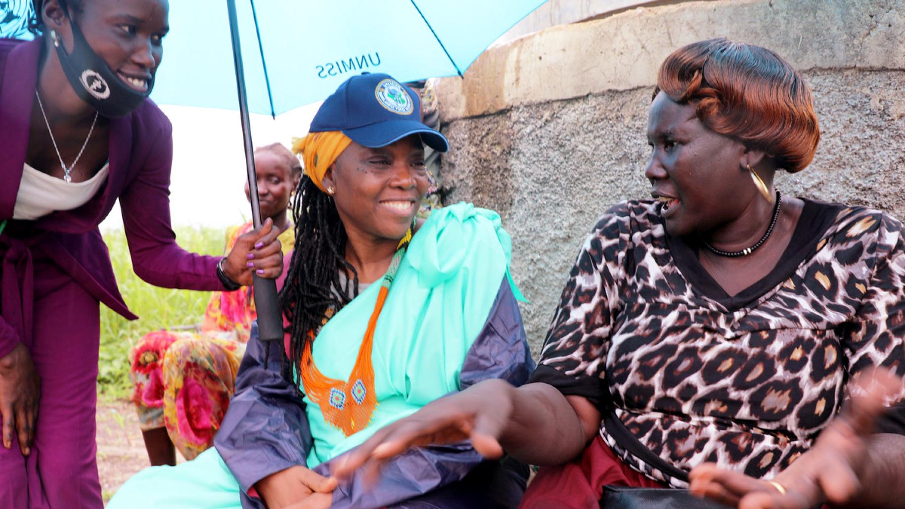 two women sit talking to each other under an umbrella