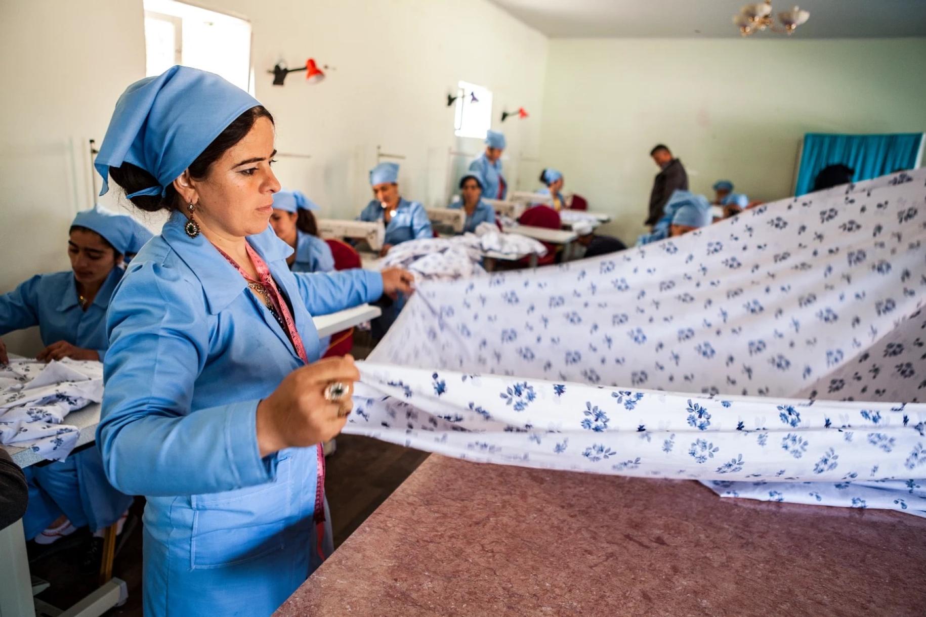 woman in blue overalls and headscarf folds a piece of cloth 