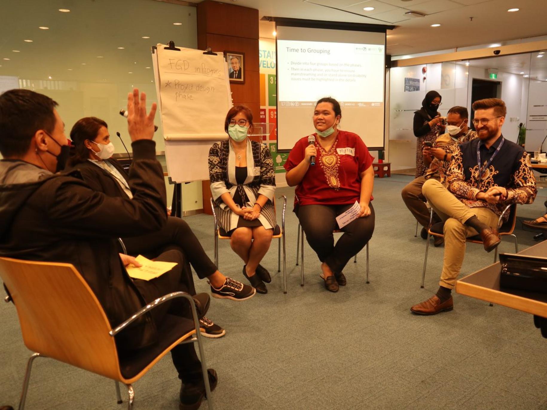 Five persons talking while sitting in chairs in a circle with a flipchart to their side