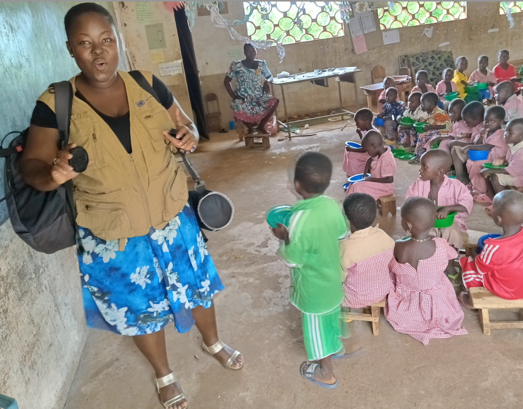 : Damba Nikabou standing in an early childhood classroom with numerous children and a teacher