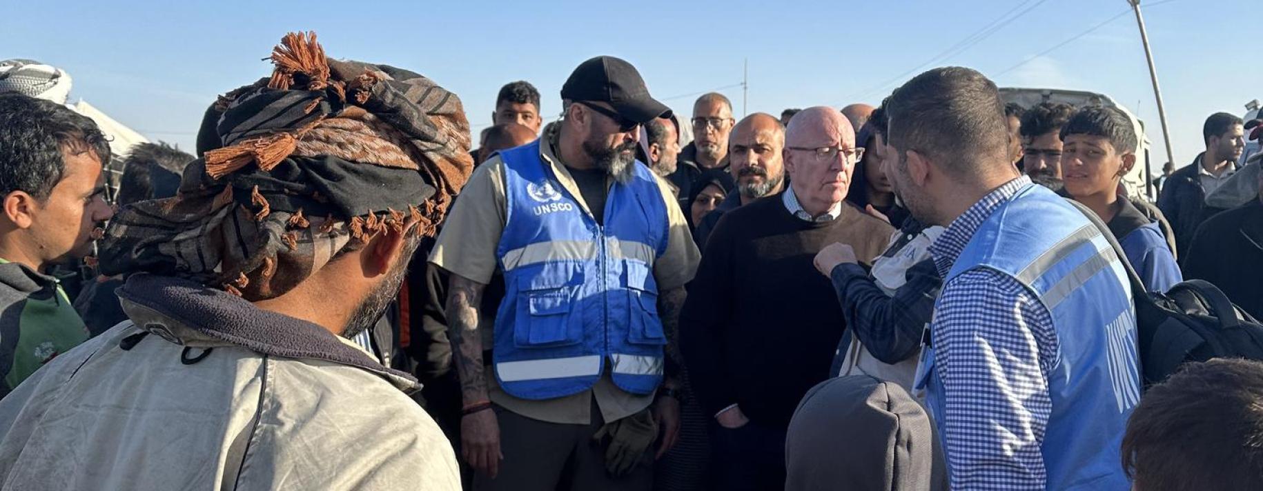 A group of men in blue bulletproof vests and grey and black shirts talk to each other in Gaza