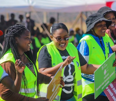 A group of participants in bright vests hold signs promoting Sustainable Development Goals while taking part in an outdoor community event.